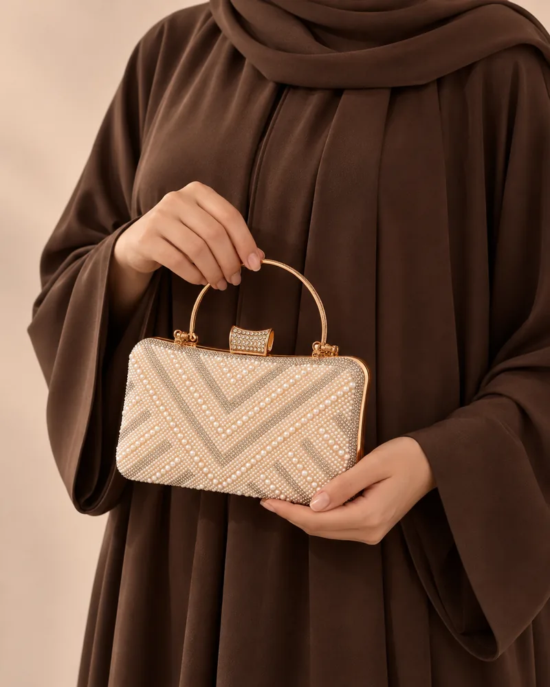 كلاتش سهرة علبة باللؤلؤ والستراس بنقشة شيفرون باللون الذهبي مع موديل محجبة تمسكها باليد