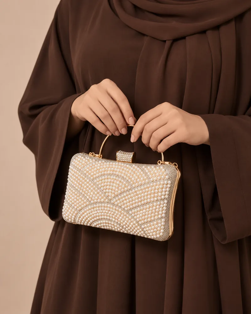 كلاتش سهرة علبة باللؤلؤ بنقشة أقواس باللون الذهبي مع موديل محجبة تمسكها باليد